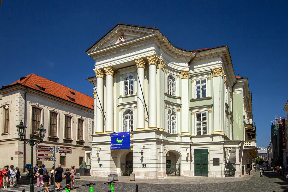 The cream and pale green neoclassical front of the Estates Theatre with white columns, under a deep blue sky.